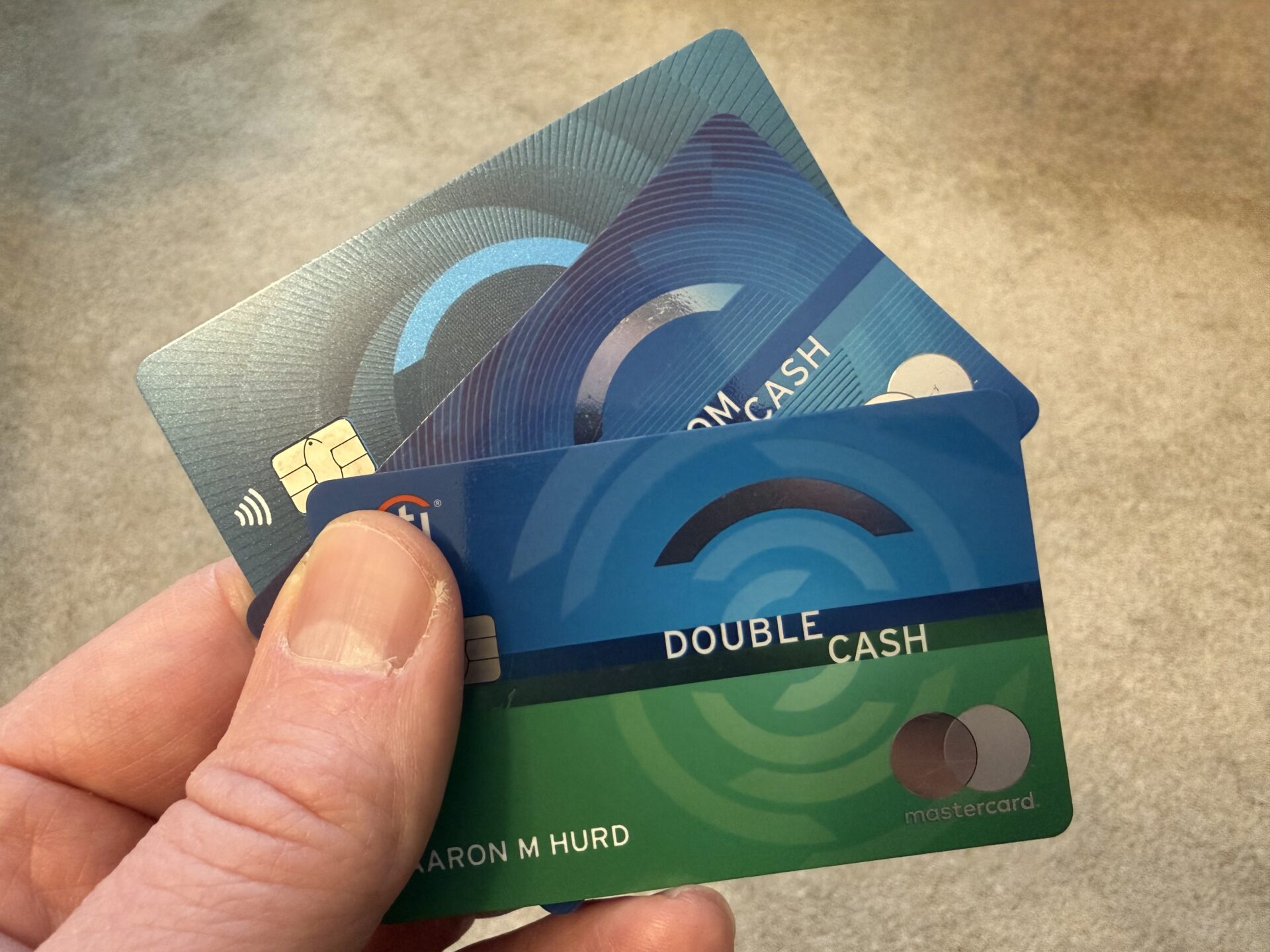 Three Citi cards being held in a person's hand. Cards are the Citi Double Cash, Citi Custom Cash, and Citi Rewards+